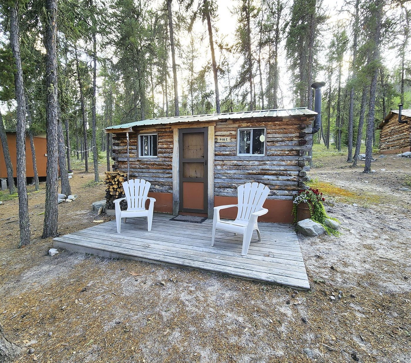 Log guest cabin with a deck and chairs among the pines at Plaisted Camps