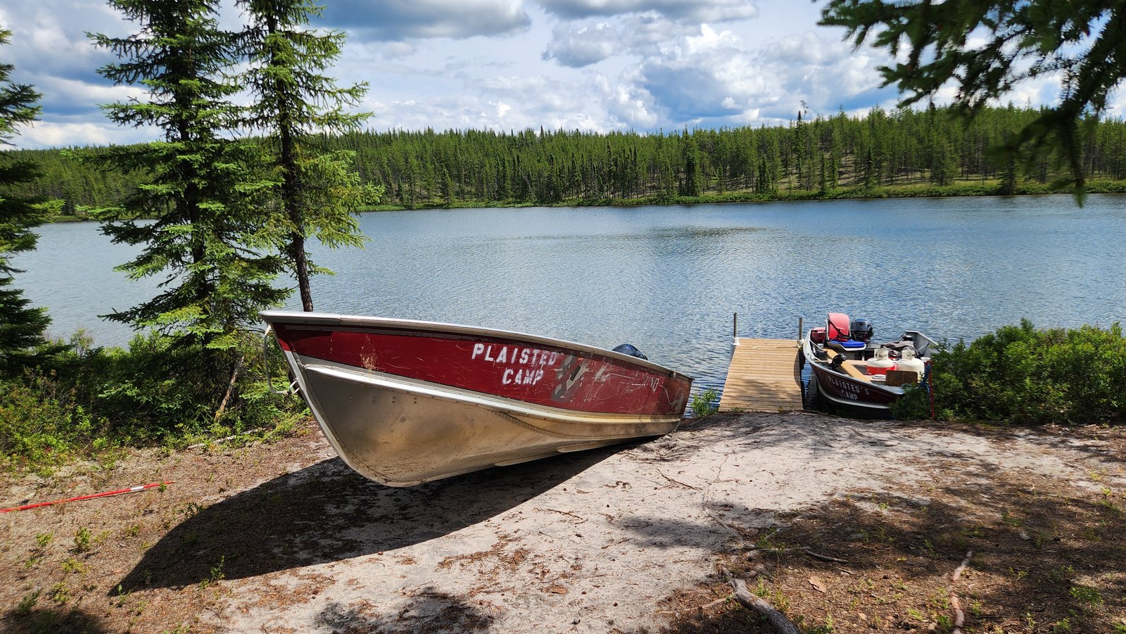 A Plaisted Camps boat on the shore beside the dock at the Wheeler River Outcamp