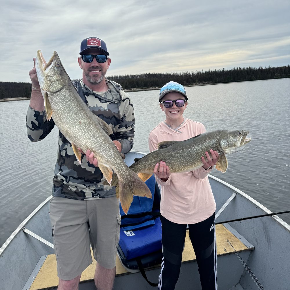An angler and a young angler each holding a lake trout in a boat in northern Saskatchewan