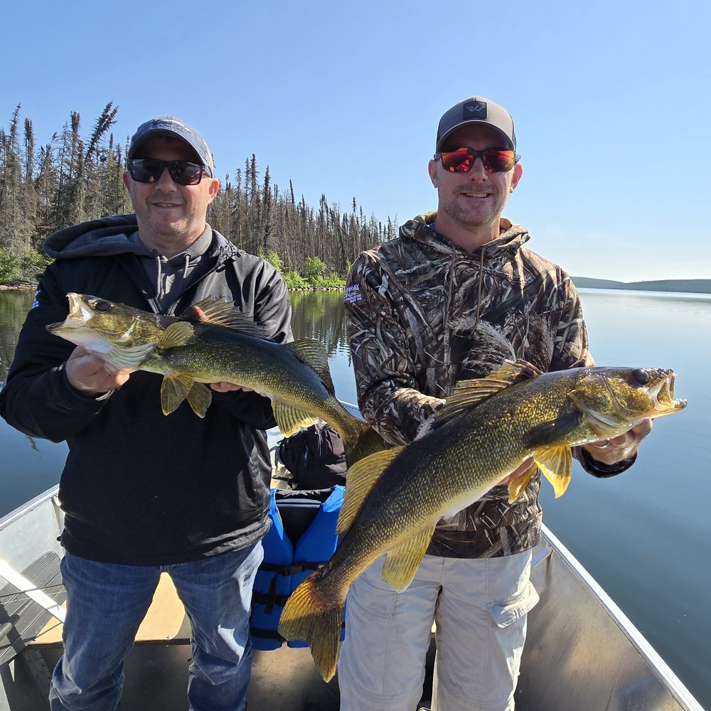 Two anglers each holding a walleye in a boat on a calm lake in northern Saskatchewan